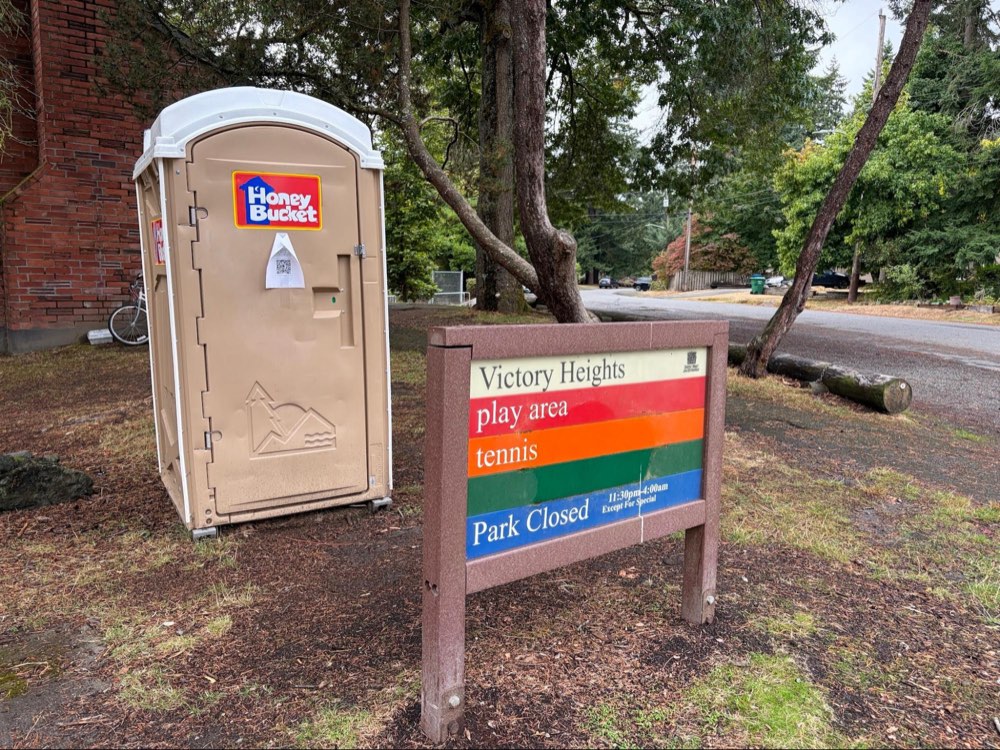 The Honey Bucket portable toilet beside the Victory Heights park sign.