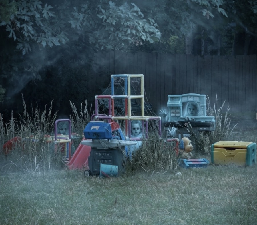 Abandoned plastic playground toys half-swallowed by tall grass at dusk, pale children's faces showing between them.